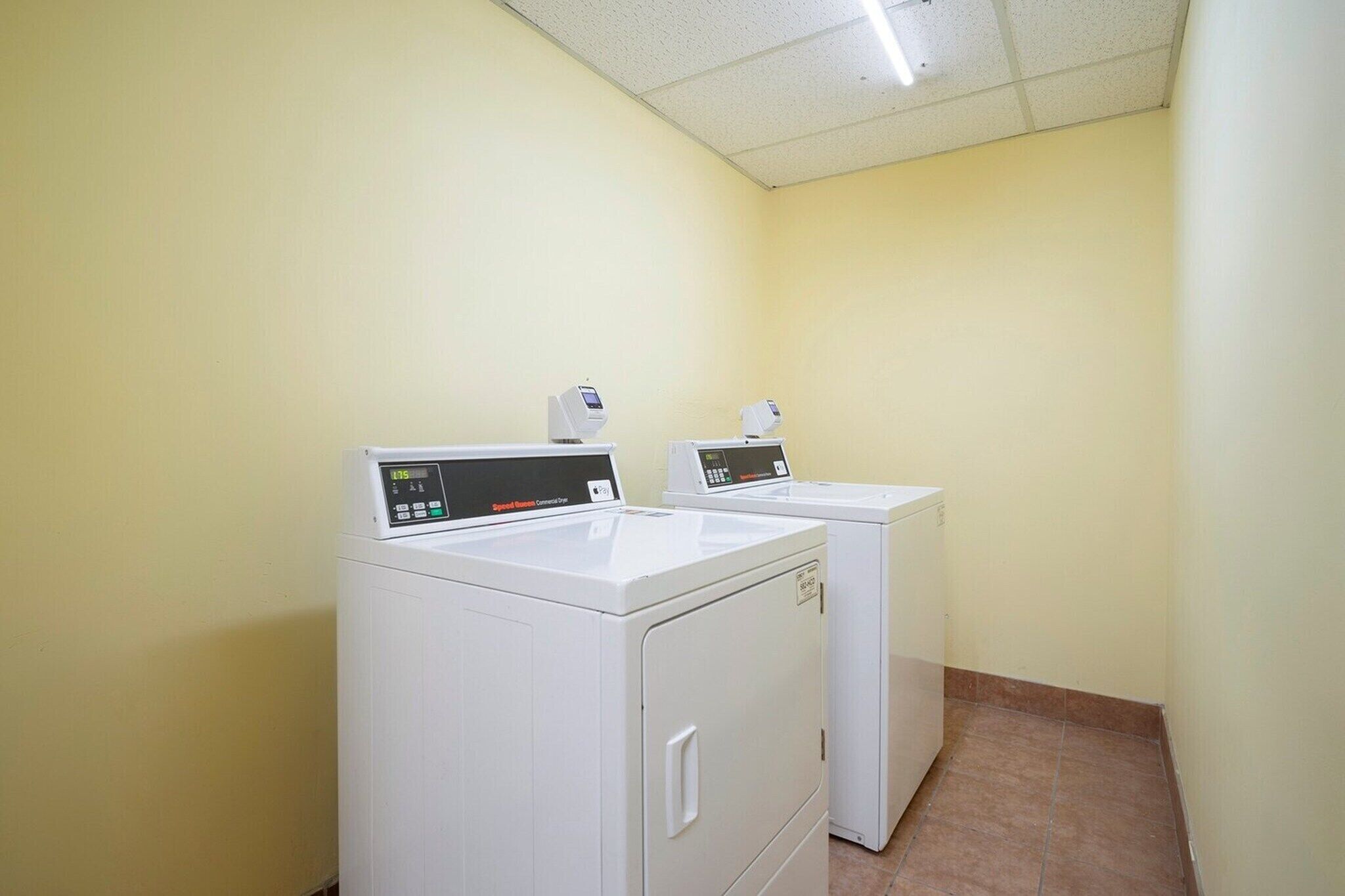 A laundry room with two white front-loading washers and dryers, a tiled floor, and a plain yellow wall.