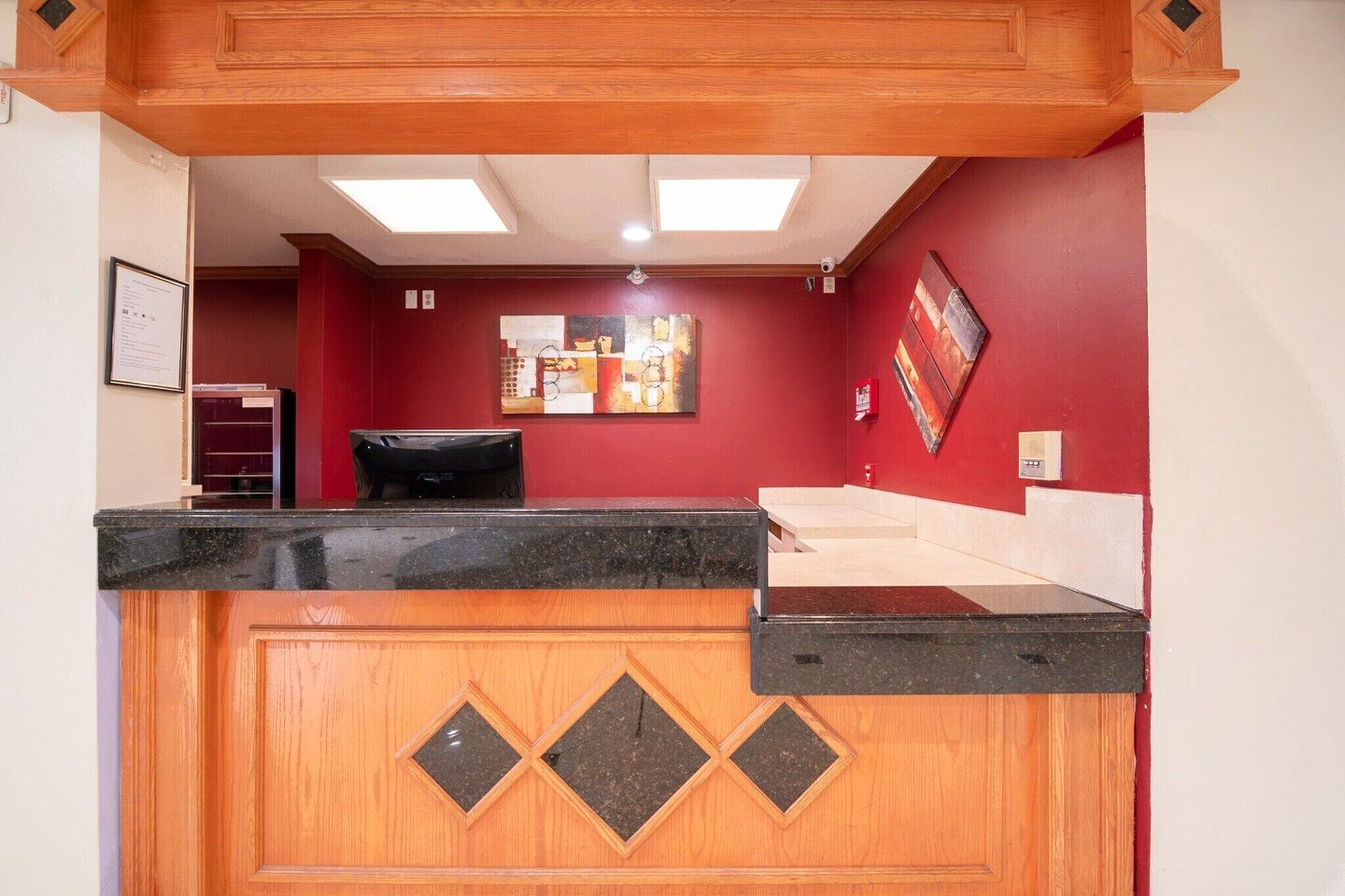 A reception desk with a wooden panel design, a black countertop, and a red wall with artwork.