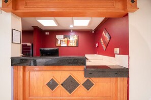 Un mostrador de recepción con paneles de madera, encimera negra y pared roja decorada con obras de arte.