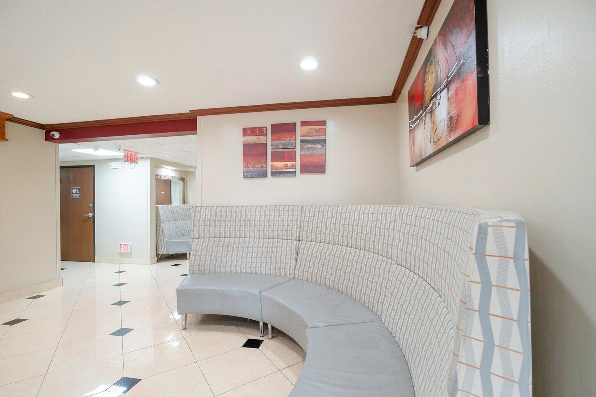 A curved sectional sofa in a hotel lobby with a tiled floor, a painting on the wall, and an exit sign.