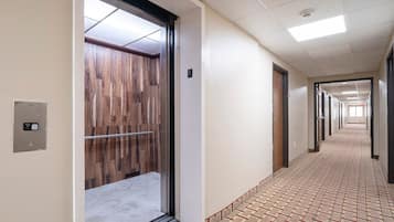 A hallway with a patterned floor, an elevator with a wooden panel door, and a ceiling with recessed lighting.