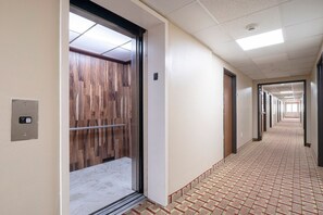 A hallway with a patterned floor, an elevator with a wooden panel door, and a ceiling with recessed lighting. - King Bed Accessible Non-Smoking (Houston)