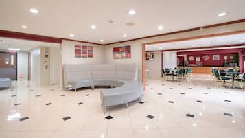 A hotel lobby with a curved seating area, a reception desk, and a dining area with tables and chairs.
