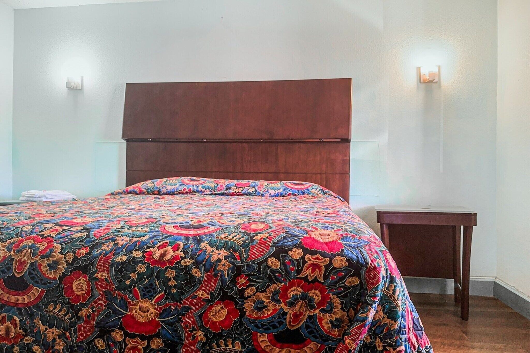 Ein Schlafzimmer mit einem großen Bett, einem Holzkopfteil, einem kleinen Nachttisch und zwei Wandlampen.