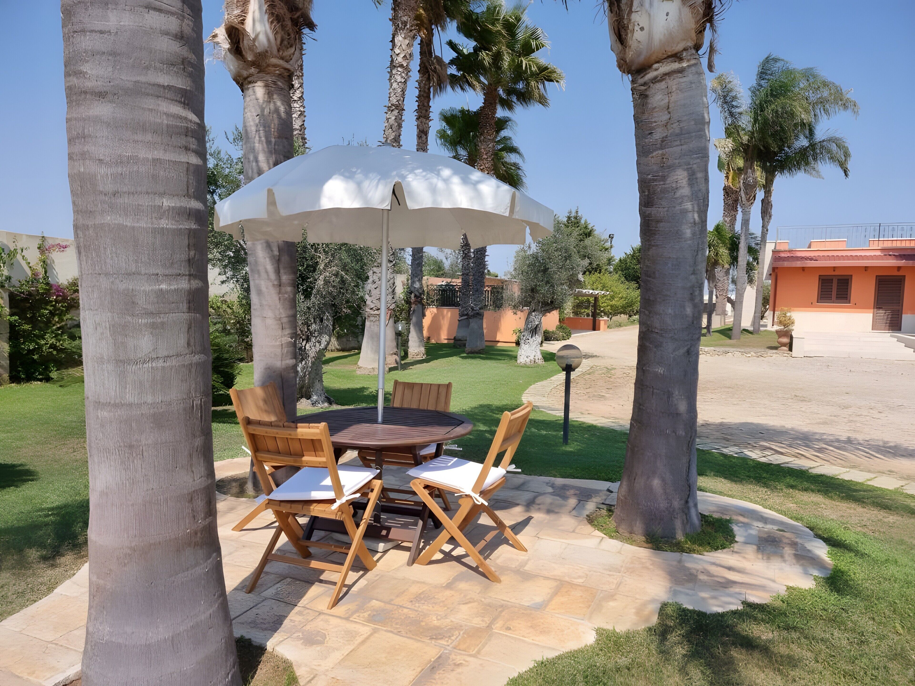 Un patio con un tavolo rotondo e sedie, un ombrellone e palme.