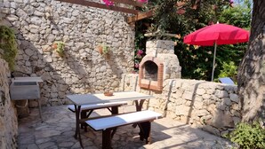 An outdoor patio with stone walls, a wooden table, benches, and a red umbrella. - Villa Giusy: Pool and Relaxation in Salento (Galatina)