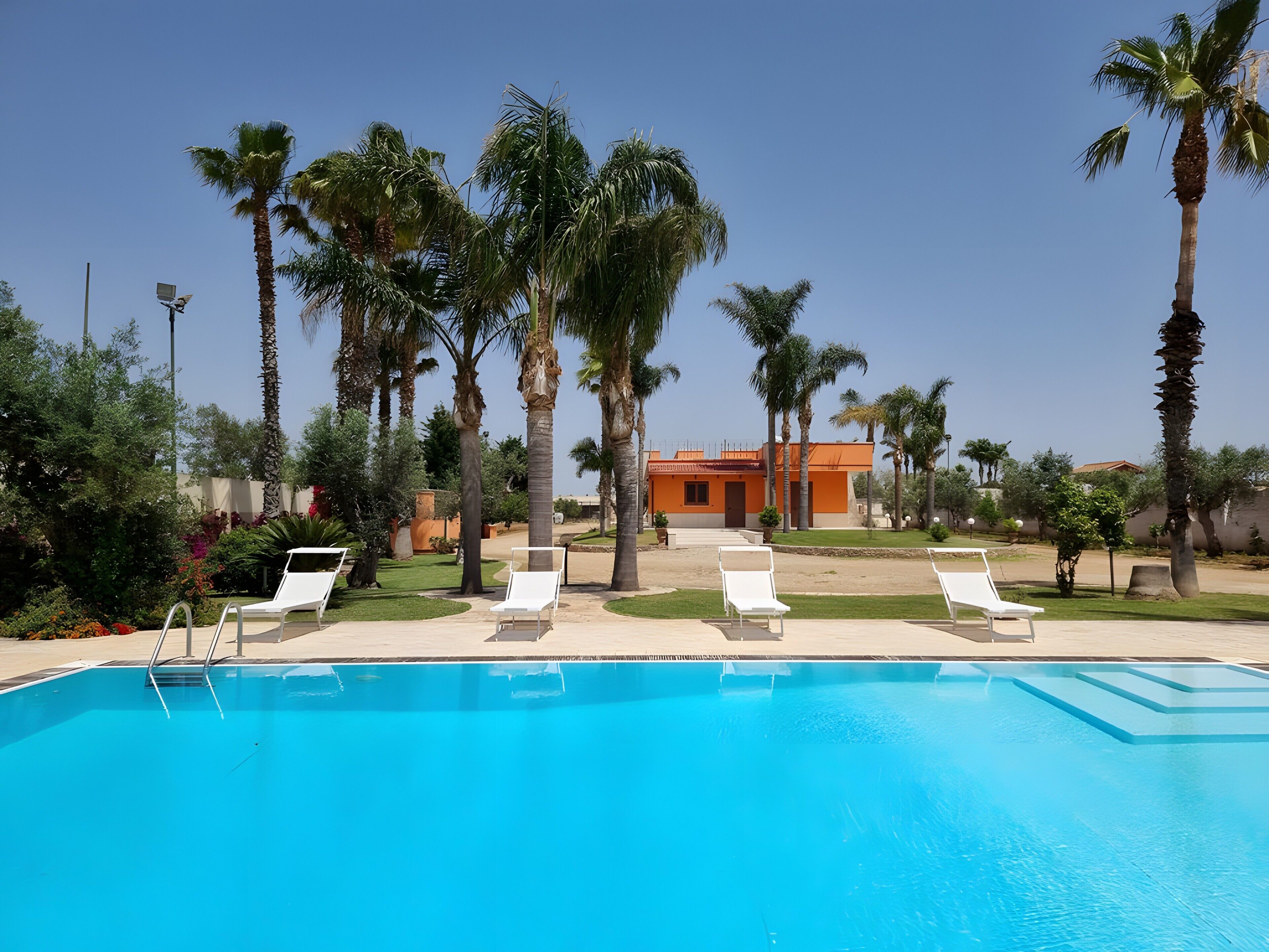 Una piscina con lettini, palme e un edificio sullo sfondo.