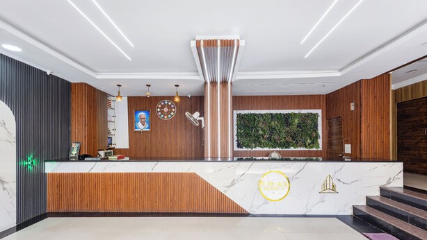 A hotel reception area with a marble counter, wooden paneling, a green wall with plants, and a staircase. - SRINIVASA RESIDENCY (Tirupati)