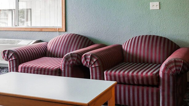 Une pièce avec deux fauteuils à rayures, une table en bois et une fenêtre avec des stores.