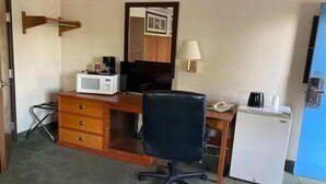 Une chambre d’hôtel équipée d’un bureau en bois, d’un fauteuil de bureau noir, d’un four à micro-ondes, d’un réfrigérateur, d’une machine à café, d’une lampe et d’un miroir.