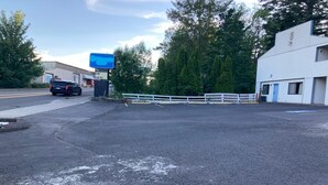Un parking délimité par une clôture blanche, un bâtiment avec une enseigne bleue et un camion garé sur le côté gauche.