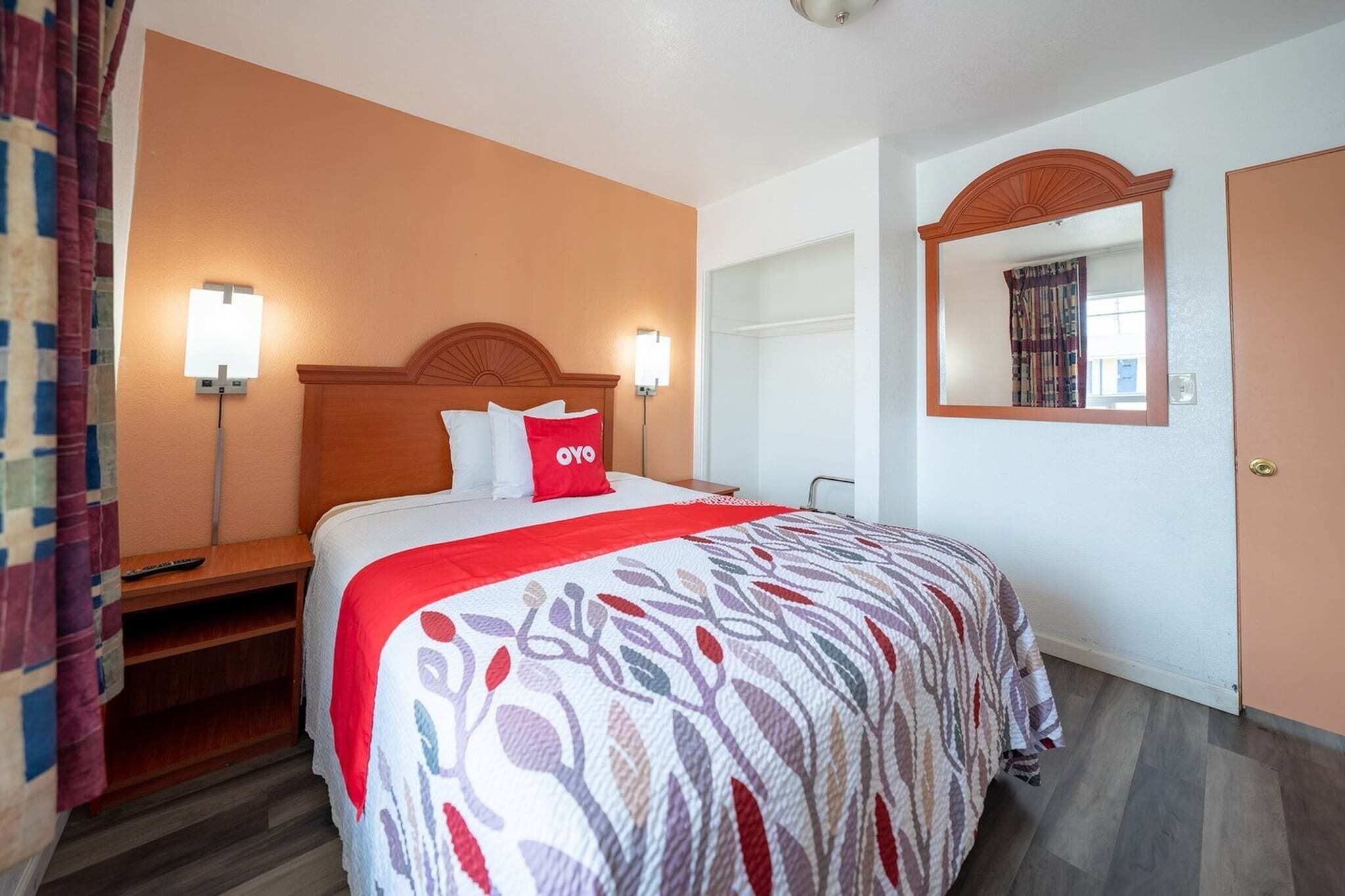 Hotellihuone, jossa on sänky, yöpöytälamput, peili ja ovi.