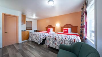 Ein Hotelzimmer mit zwei Betten, einem Schreibtisch, einem Stuhl und einem fensterbepflanzten Fenster.