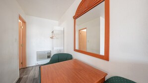 A small room with a wooden table, two green chairs, a large mirror, and a radiator. - Premium Queen Bed|Kitchenette (Madras OR)