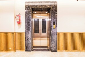 An elevator with a fire extinguisher on the wall, a control panel, and a wooden panel design on the floor. - Palette Shree Jagannath Puri (Puri)