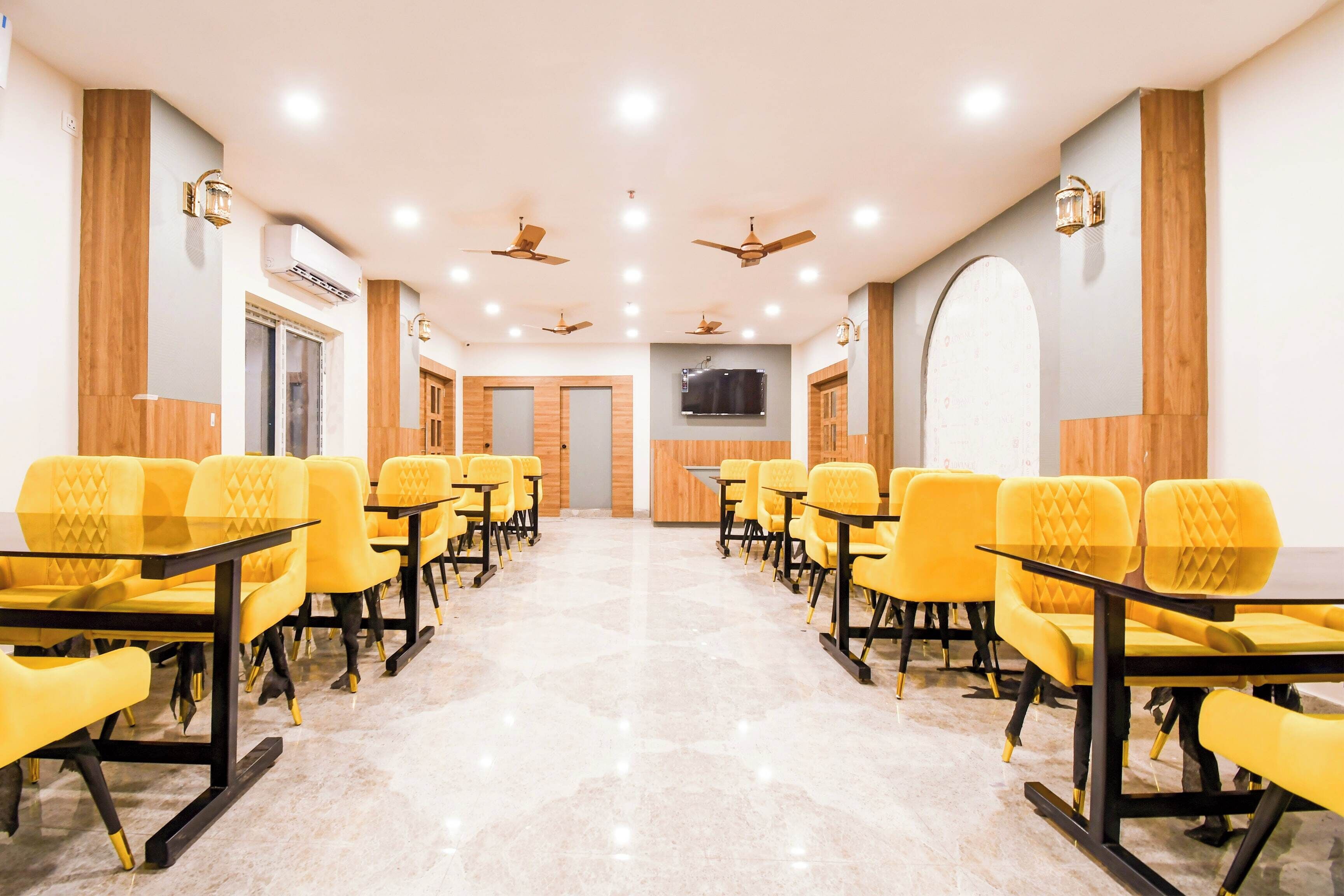 A conference room with yellow chairs and tables, ceiling fans, and a flat-screen TV on the wall.