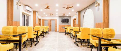 A conference room with yellow chairs and tables, ceiling fans, and a flat-screen TV on the wall.