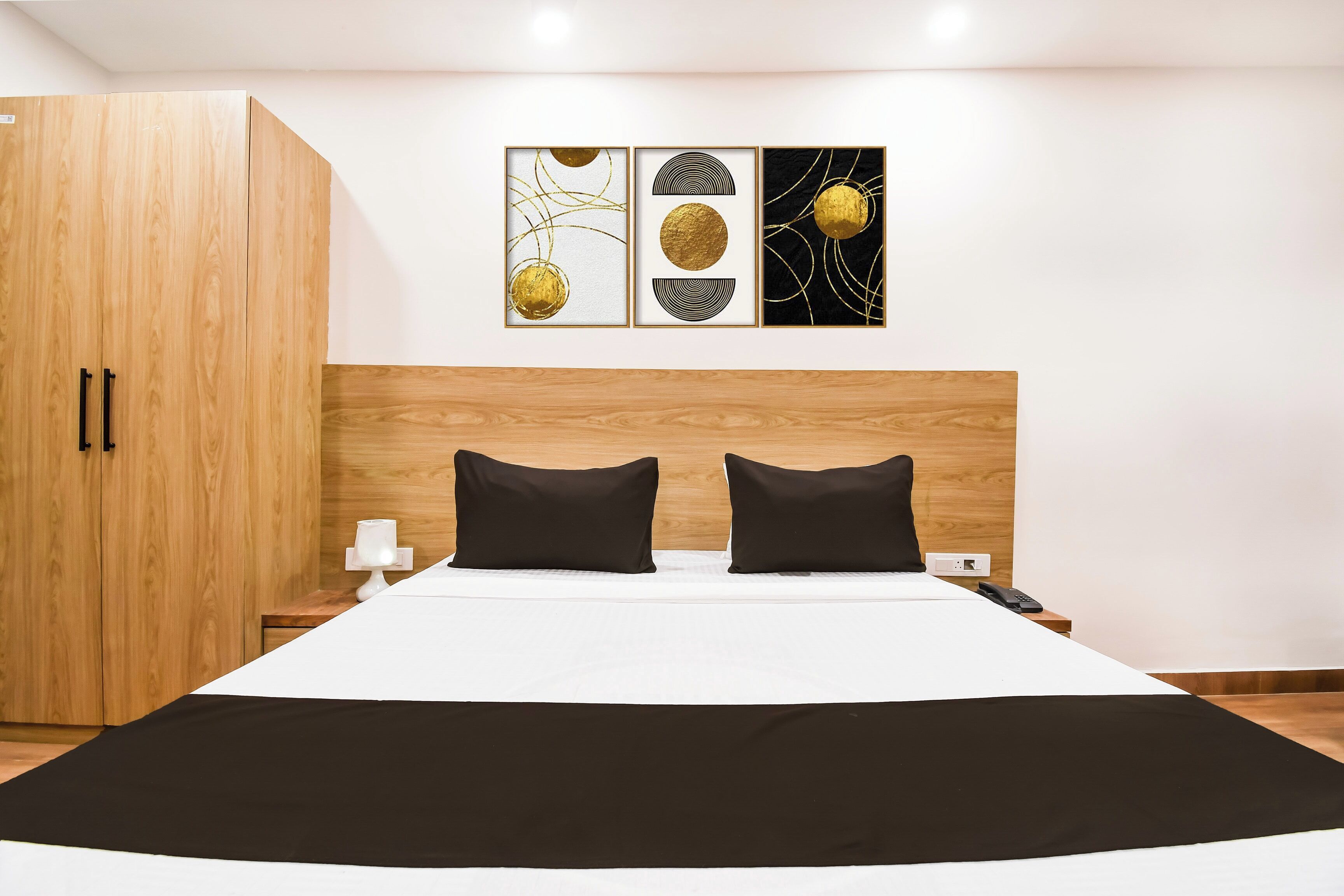 Ein Schlafzimmer mit einem Bett, zwei schwarzen Kissen, einem Nachttisch mit einer Lampe, einem Telefon und einer Wand mit drei gerahmten Kunstwerken.
