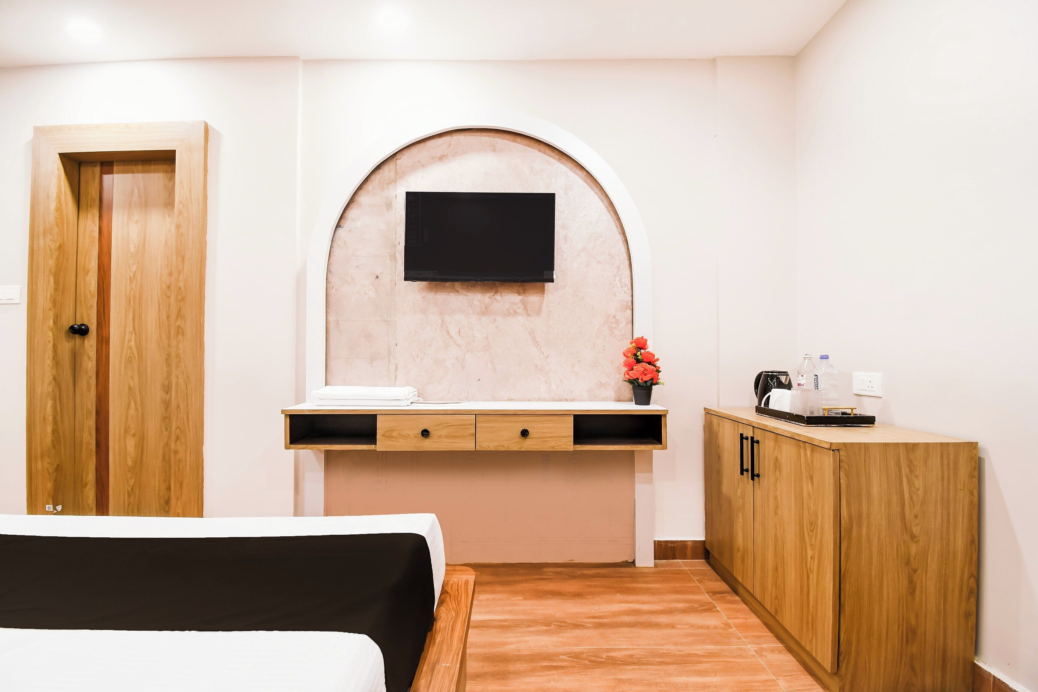 A hotel room with a bed, a wooden wardrobe, a desk with a flat-screen TV, and a small potted plant.