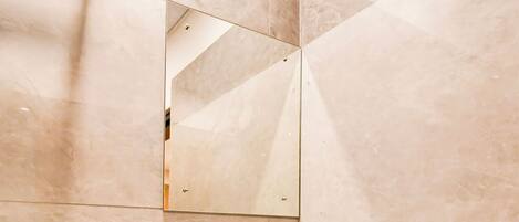 Un baño con un lavamanos blanco, un espejo y paredes cubiertas de azulejos color beige.