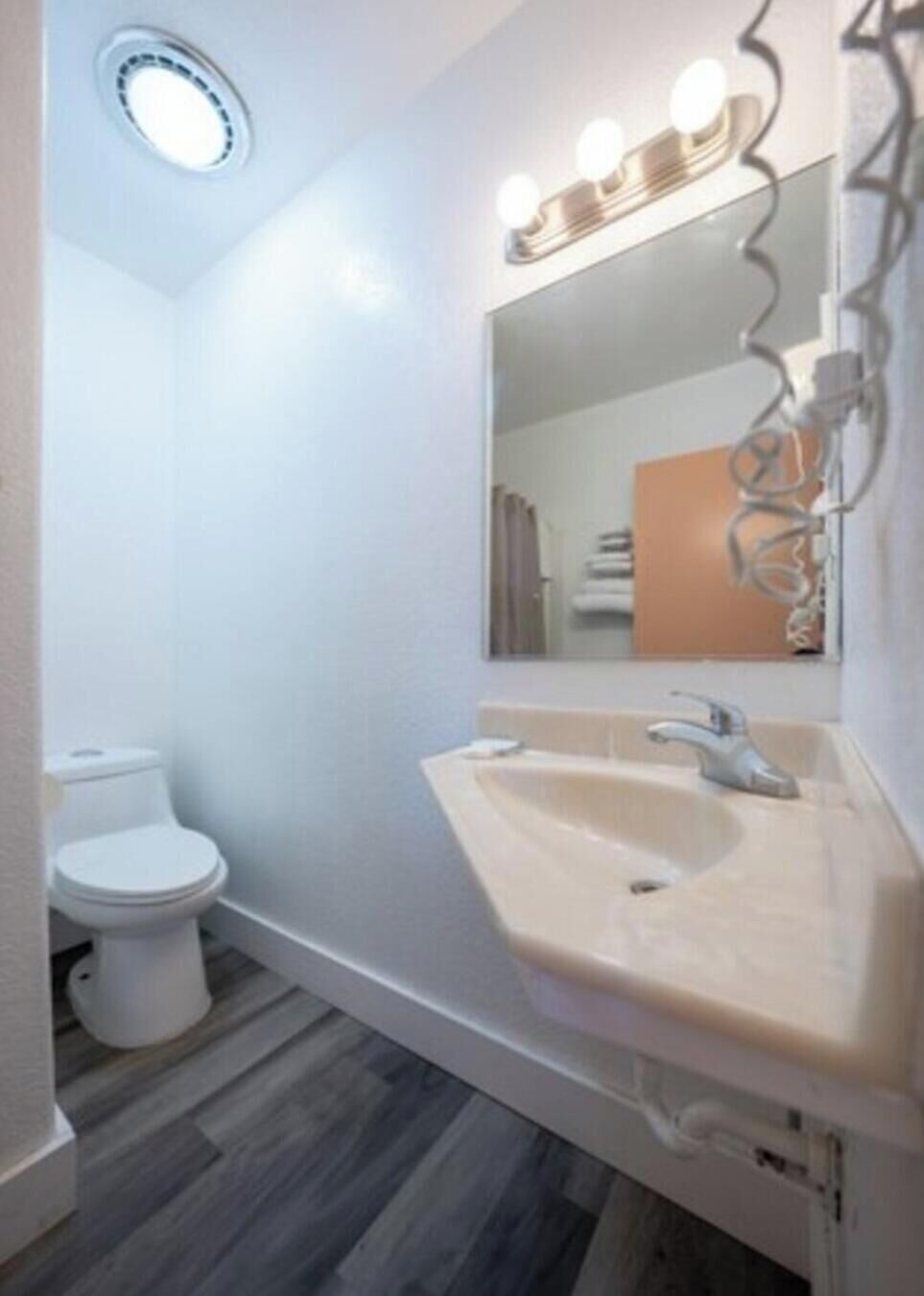 Une salle de bain avec des toilettes blanches, un lavabo beige et un miroir avec éclairage intégré.