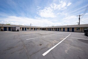 A motel with a large parking lot, multiple rooms, and a utility trailer. - Premium 2 Queen Bed|Kitchenette (Madras OR)
