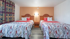 A hotel room with two beds, each with a patterned bedspread and a red pillow with 'OYO' branding.