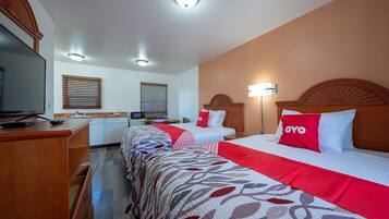 A hotel room with two beds, a desk, a television, and a window with blinds.