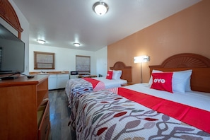 Habitació d'hotel amb dos llits, un escriptori, una televisió i una finestra amb persianes.