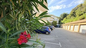 A parking area with cars, a building with balconies, and a plant with red flowers. - Montpellier Sunlight, Air Conditioning, Pool, and Private Parking (Montpellier)
