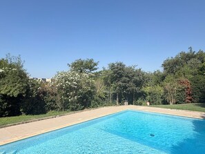 Piscina retangular com água azul cristalina, rodeada por um deck ladrilhado e vegetação exuberante.