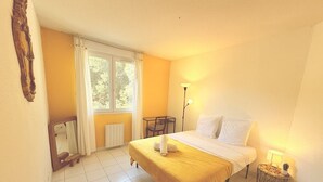 A hotel room with a bed, a chair, a table, a lamp, and a window with curtains. - Montpellier Sunlight, Air Conditioning, Pool, and Private Parking (Montpellier)