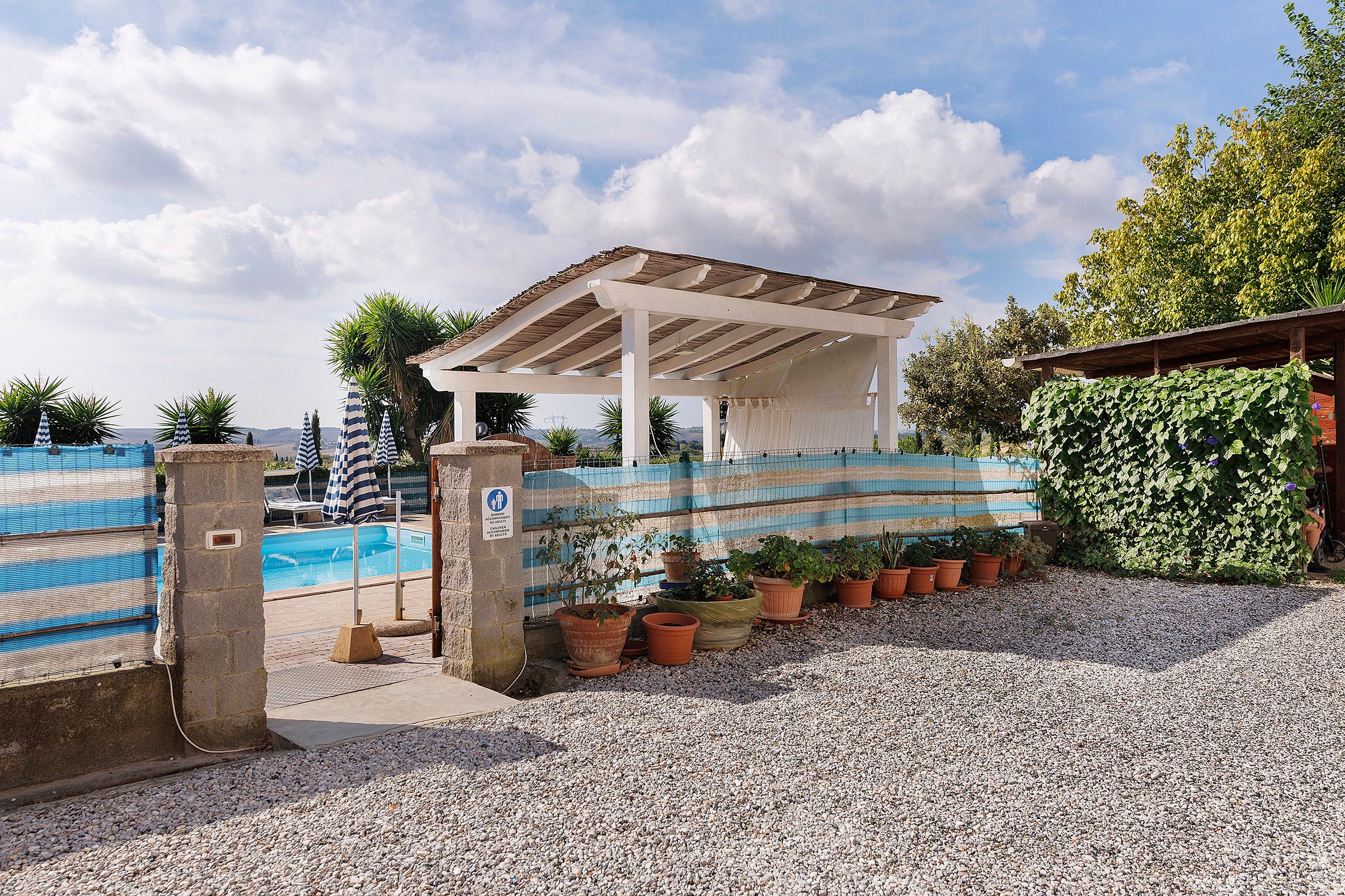 A pool area with a covered seating area, a fenced pool, and potted plants.