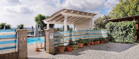 A pool area with a covered seating area, a fenced pool, and potted plants.