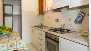 Eine Küche mit Gasherd, Backofen und Spüle. Ein Tisch mit Tischdecke und einer Blumenschale.