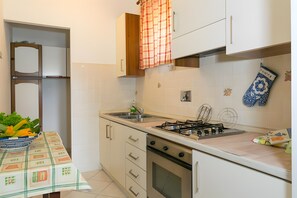 A kitchen with a gas stove, oven, and sink. There is a table with a placemat and a bowl of flowers. - Apartment 'Agriturismo Case Nuove - Sole' with Shared Pool, Wi-Fi and Air Conditioning (Castellina Marittima)