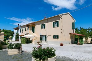 A two-story building with a staircase, outdoor seating, and potted plants. - Apartment 'Agriturismo Case Nuove - Sole' with Shared Pool, Wi-Fi and Air Conditioning (Castellina Marittima)
