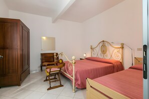 A bedroom with a wooden wardrobe, a rocking chair, a bed with a decorative headboard, and a bedside table with a lamp. - Apartment 'Agriturismo Case Nuove - Sole' with Shared Pool, Wi-Fi and Air Conditioning (Castellina Marittima)