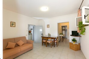 A living room with a sofa, a dining table with chairs, a TV on a stand, and a kitchen area in the background. - Apartment 'Agriturismo Case Nuove - Sole' with Shared Pool, Wi-Fi and Air Conditioning (Castellina Marittima)
