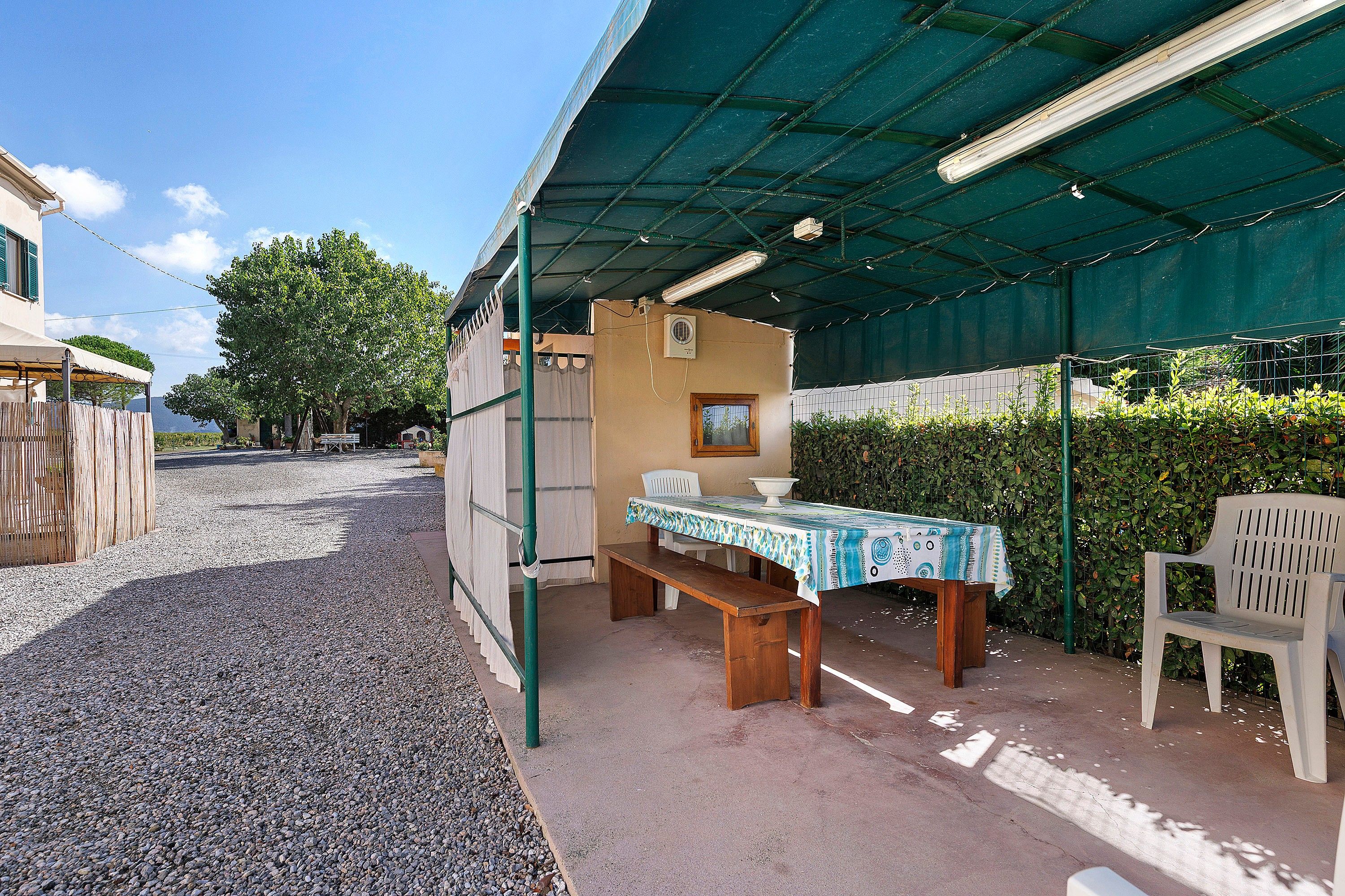 An outdoor patio area with a table and chairs, a covered seating area, and a gravel path leading to a building.