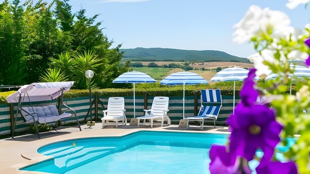 Ein Poolbereich mit Liegestühlen und Sonnenschirmen, umgeben von Grünpflanzen und Hügeln im Hintergrund.