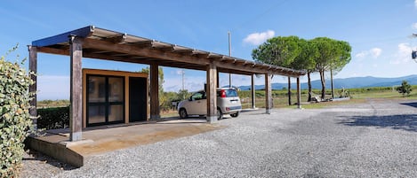 A covered outdoor area with a car parked under a pergola, gravel ground, and a clear sky.