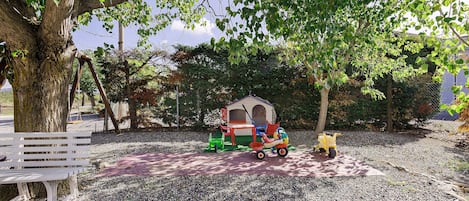 Un parque con una casita de juegos, un banco y un cochecito.