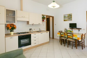 A compact kitchen with a dining area, a TV, and a painting on the wall. - Apartment 'Agriturismo Case Nuove - Girasole' with Shared Pool, Wi-Fi and Air Conditioning (Castellina Marittima)