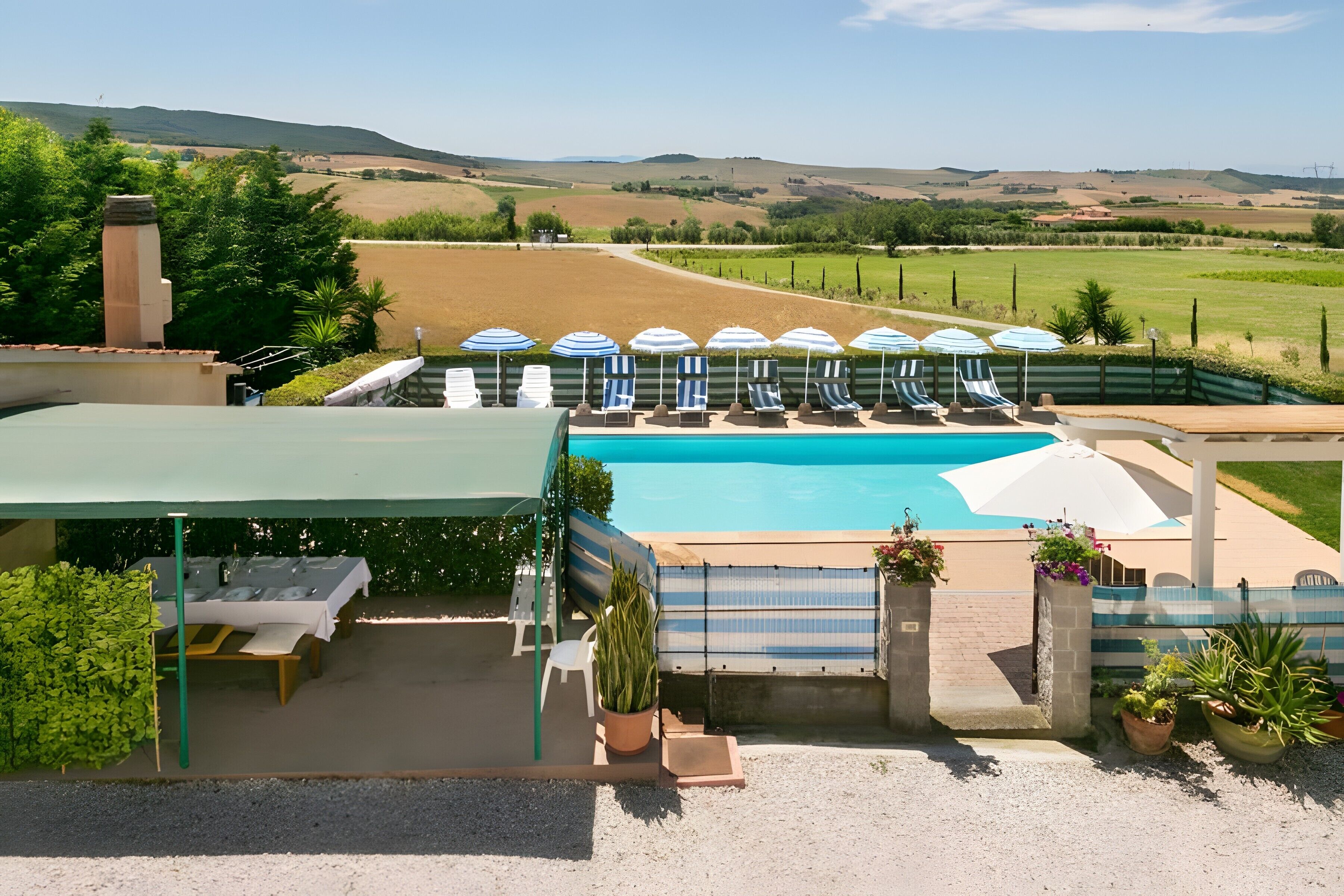 A pool area with lounge chairs and umbrellas, surrounded by a fence, with a view of the countryside.