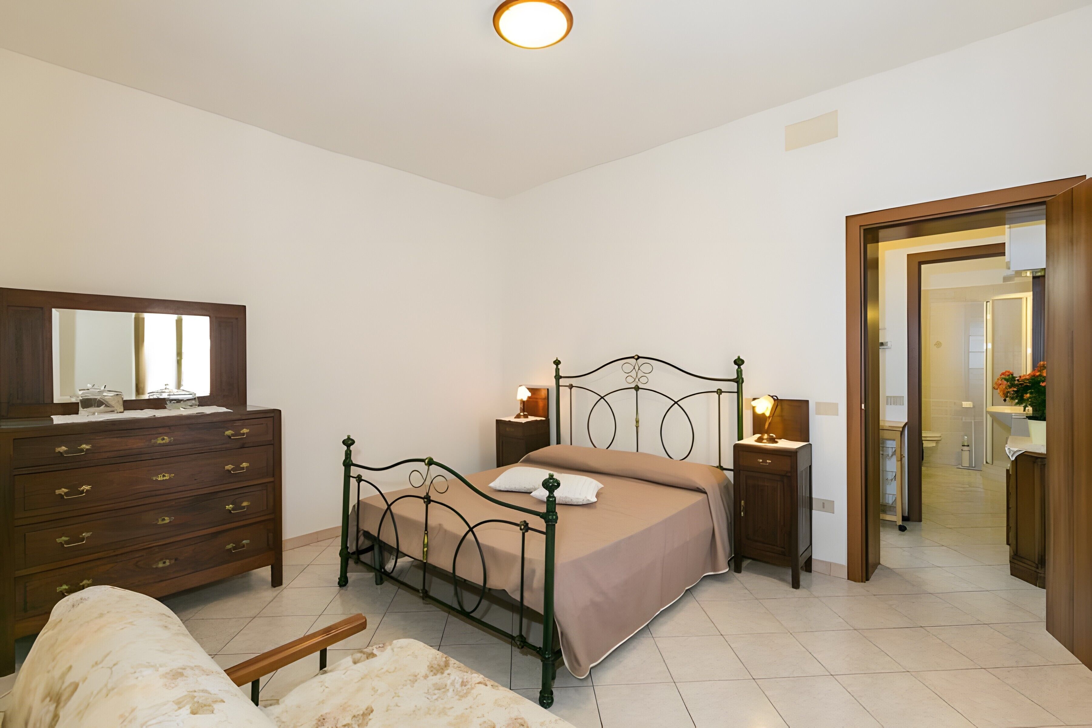 Quarto com cama, penteadeira, mesas de cabeceira e espelho.
