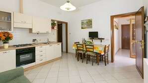 A compact kitchen with a dining area, a TV, and a door leading to another room. - Apartment 'Agriturismo Case Nuove - Girasole' with Shared Pool, Wi-Fi and Air Conditioning (Castellina Marittima)