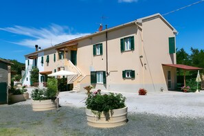 A two-story building with a flat roof, a staircase, and a covered outdoor area with umbrellas. - Apartment 'Agriturismo Case Nuove - Geranio' with Shared Pool, Wi-Fi and Air Conditioning (Castellina Marittima)