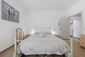 Ein schlicht eingerichtetes Schlafzimmer mit einem Bett, Nachttischlampen, einer Holzleiter und einer Tür zu einem weiteren Raum.
