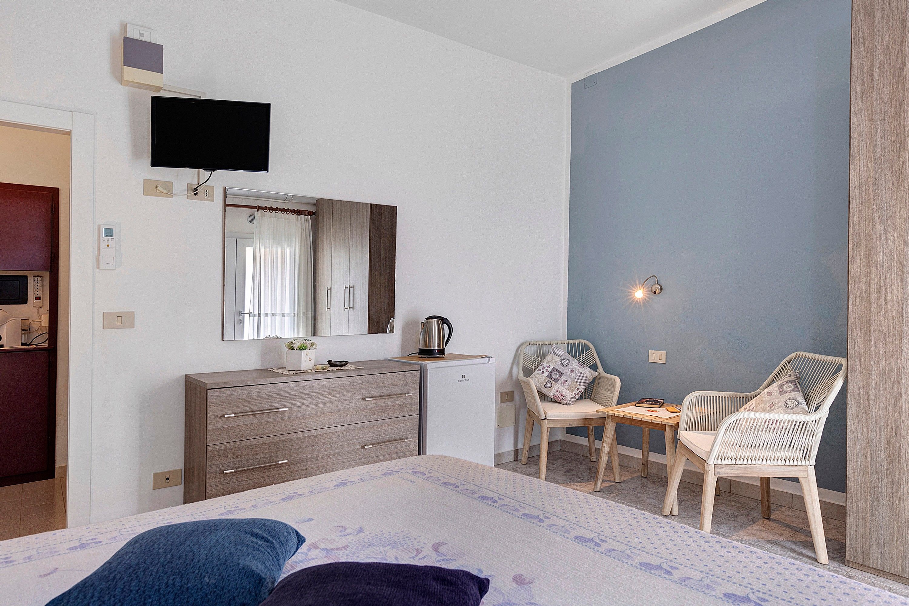 Un dormitorio con una cama, cómoda, televisor, silla y una mesita.
